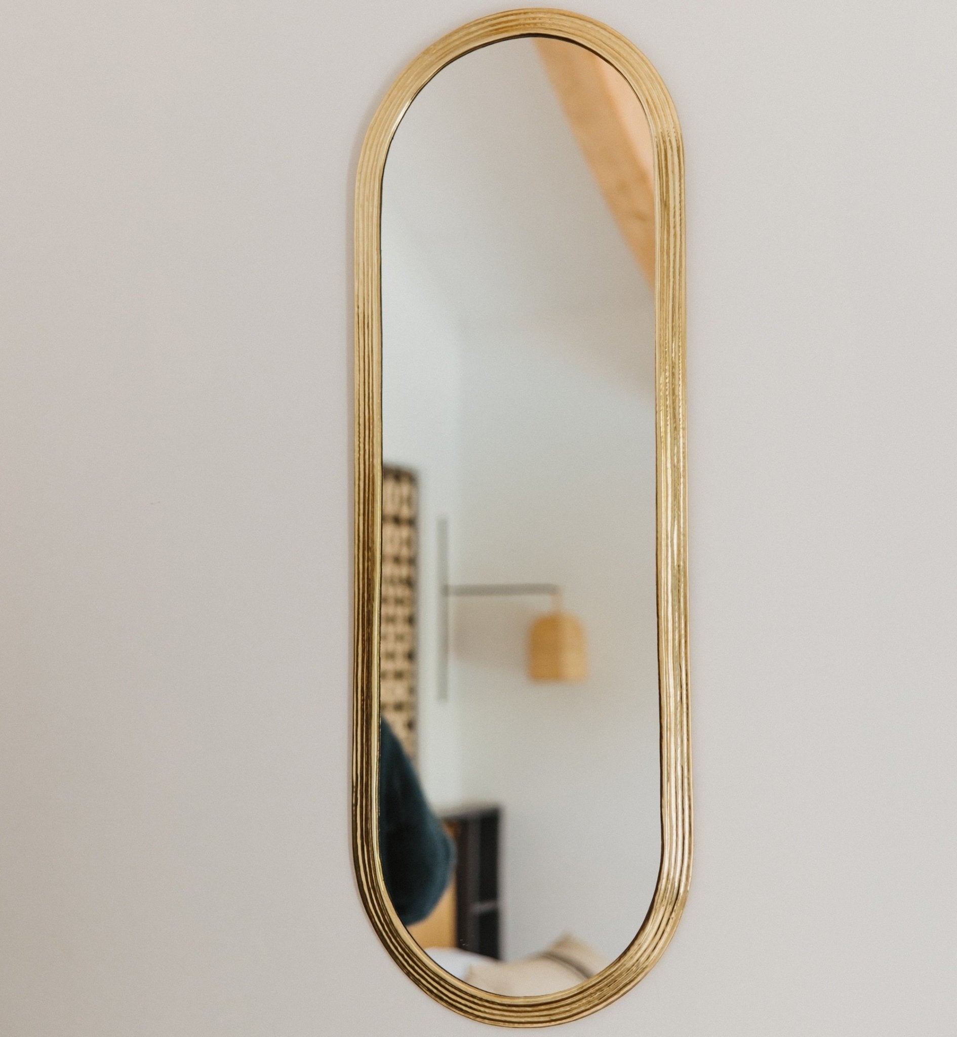 Miroir ovale en laiton doré suspendu au mur, reflétant une pièce lumineuse et élégante.