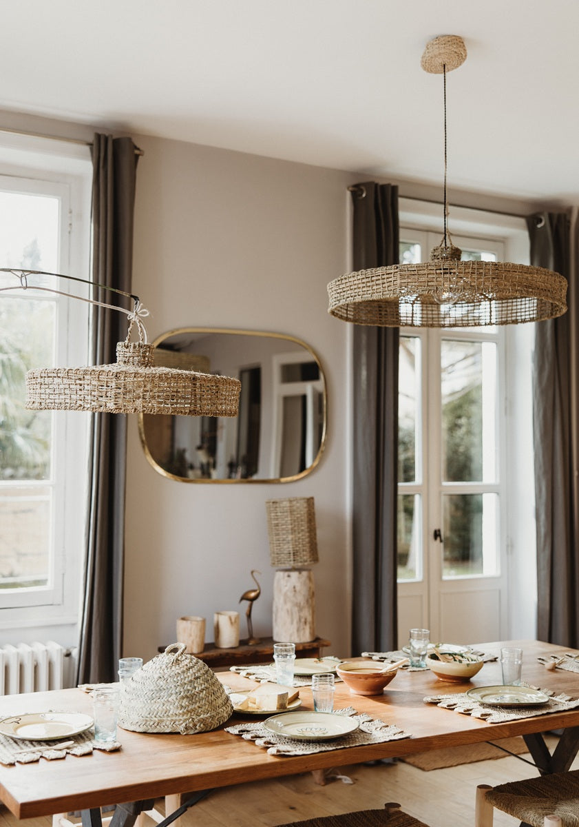 Salle à manger méditerranéenne décorée avec des objets COSYDAR-DECO faits main : suspensions tressées en fibre naturelle, miroir doré, table en bois brut, sets de table tressés, rideaux en lin