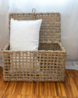 Malle de rangement tressée en corde de palmier posée au sol avec un coussin LINE