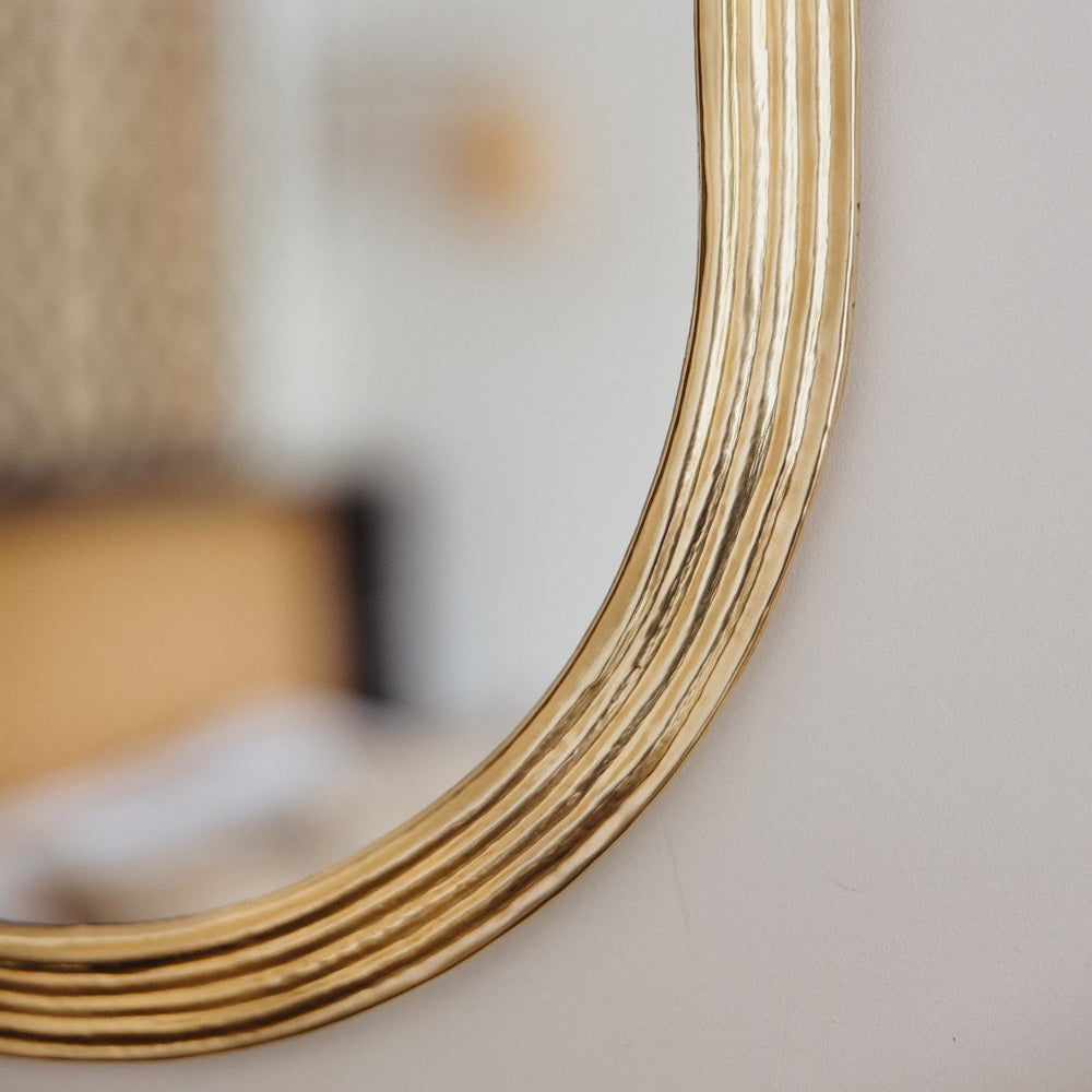 Détail du cadre martelé d’un miroir ovale en laiton doré Cosydar, finition brillante et raffinée.