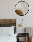 Support de lampe en métal noir avec suspension en fibre naturelle sur une table de chevet, sous un miroir rond