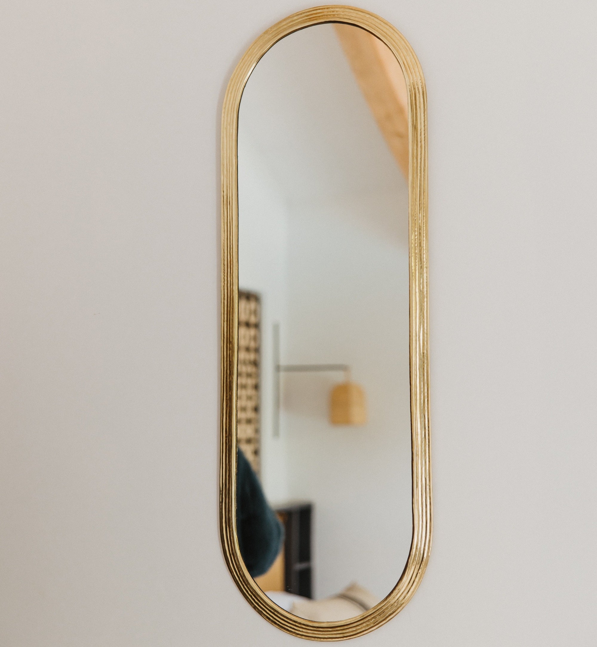 Miroir ovale en laiton doré suspendu au mur, reflétant une pièce lumineuse et élégante.
