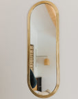 Miroir ovale en laiton doré suspendu au mur, reflétant une pièce lumineuse et élégante.