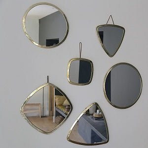 Mur décoré de miroirs en laiton doré Cosydar, formes rondes, carrées et triangulaires reflétant une ambiance naturelle et élégante