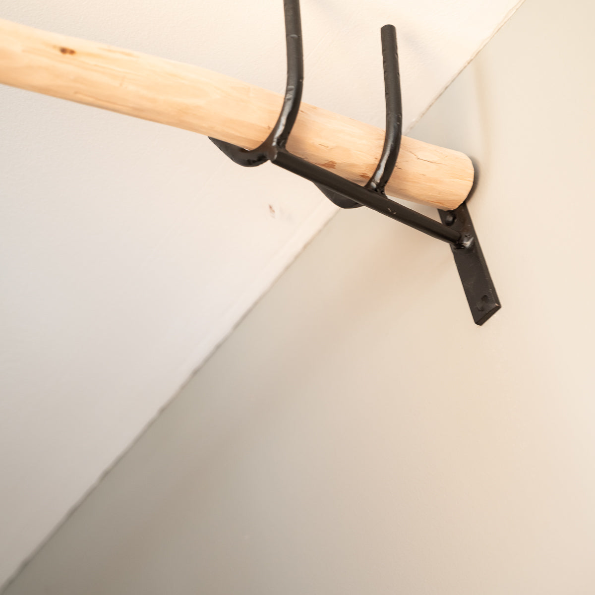 Détail support mural en V noir mat avec bâton de tringle bois clair Cosydar