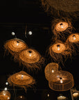 Plusieurs suspensions luminaires en fibre naturelle tressée, allumées et diffusant une lumière dorée, accrochées à différentes hauteurs dans une pièce sombre.
