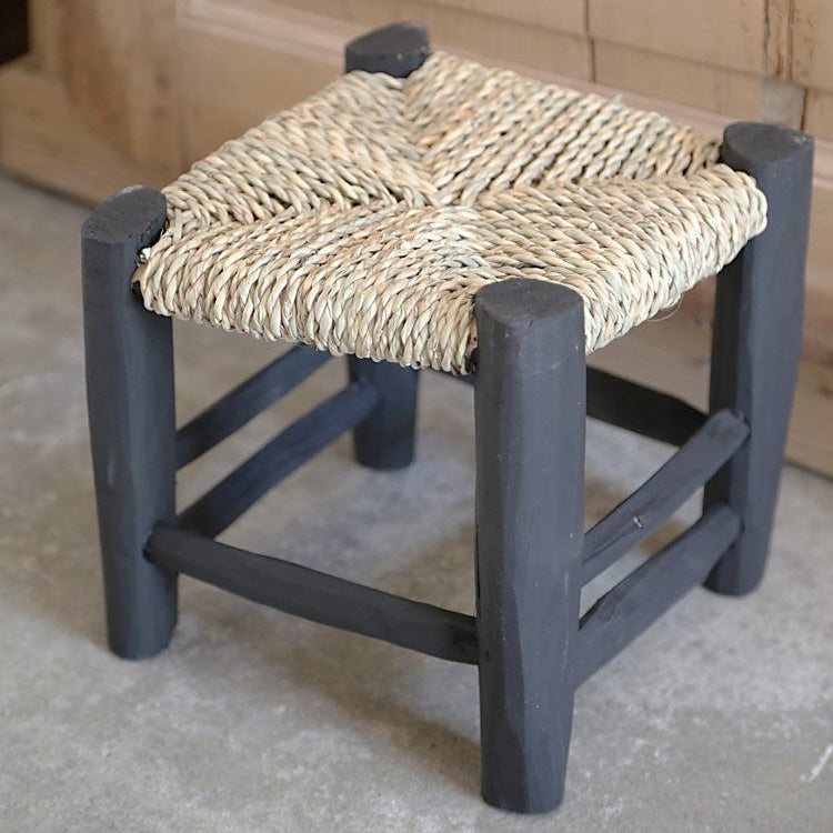 Détail du petit tabouret en bois peint en noir tressé en fibre naturelle