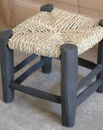 Détail du petit tabouret en bois peint en noir tressé en fibre naturelle