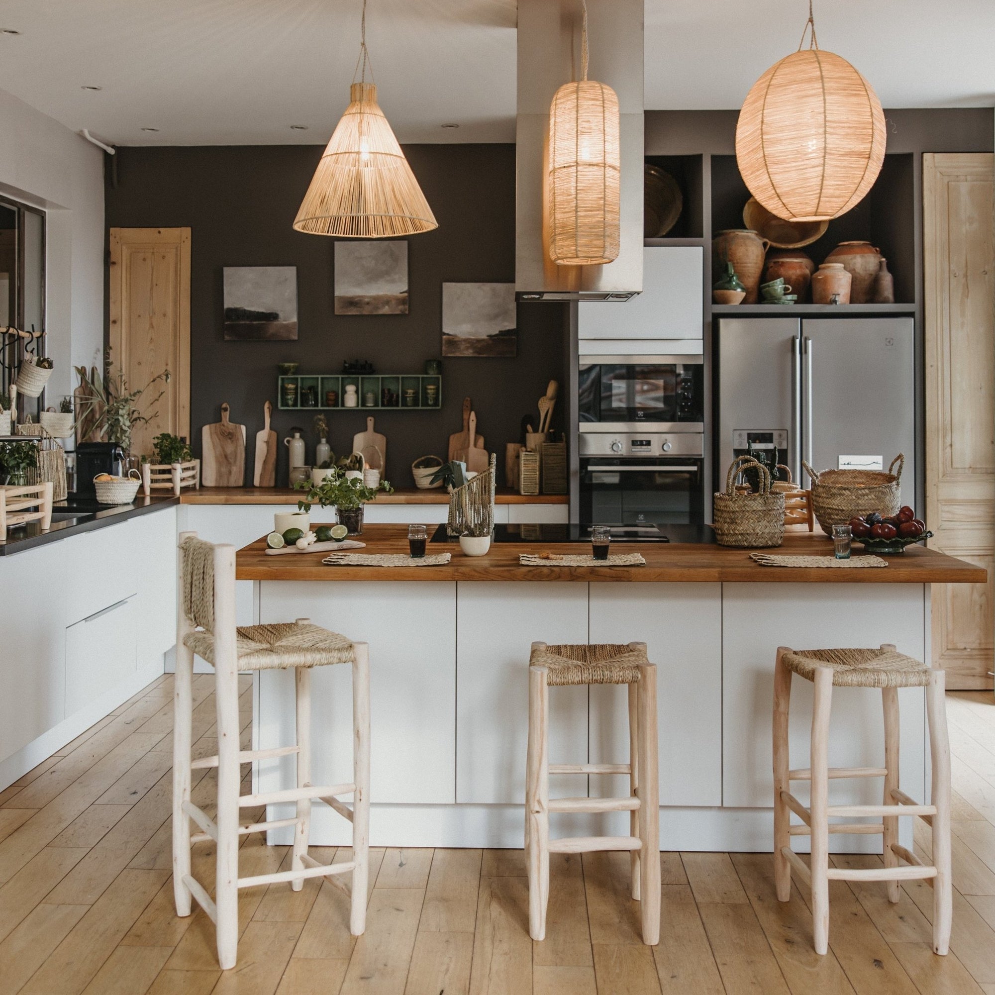 Trois suspensions raphia naturel tressées au-dessus îlot central cuisine bohème et tabourets en bois Cosydar