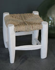 Détail du petit tabouret en bois peint en blanc tressé en fibre naturelle